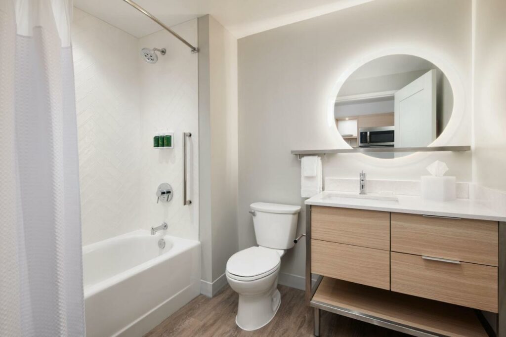 Banheiro do TownePlace Suites by Marriott Tampa Casino Area com uma banheira, um vaso sanitário, um móvel de madeira com a pia e um espelho redondo, para representar hotéis perto do Busch Gardens