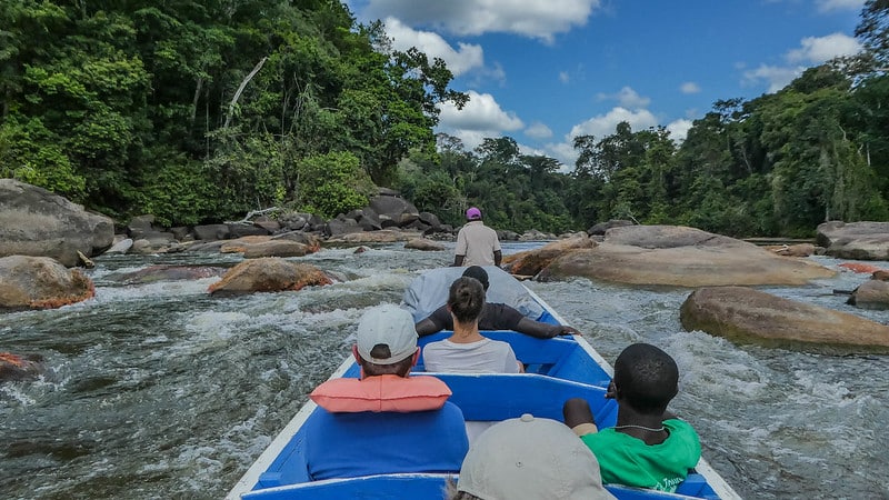Barco azul e branco com cinco pessoas dentro no meio do rio com pedras durante o dia em Suriname.