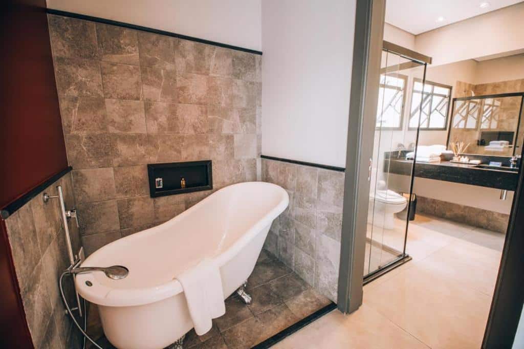 Banheiro da Villa Amistà Campos do Jordão com uma banheira com um toalha branca pendurada, há também um box  de vidro e uma pia com um espelho