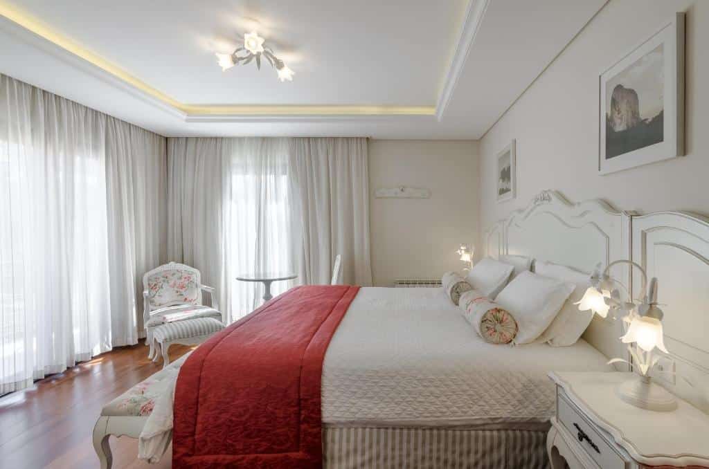 Quarto na Villa D´Biagy Premium com duas sacadas, chão de madeira, cama de casal ampla, uma poltrona, duas mesinhas de cabeceira com abajures