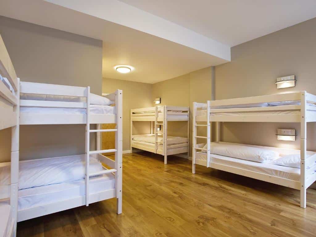 Quarto compartilhado do Wombat’s City Hostel em Londres com chão de madeira e quatro beliches brancas com travesseiros