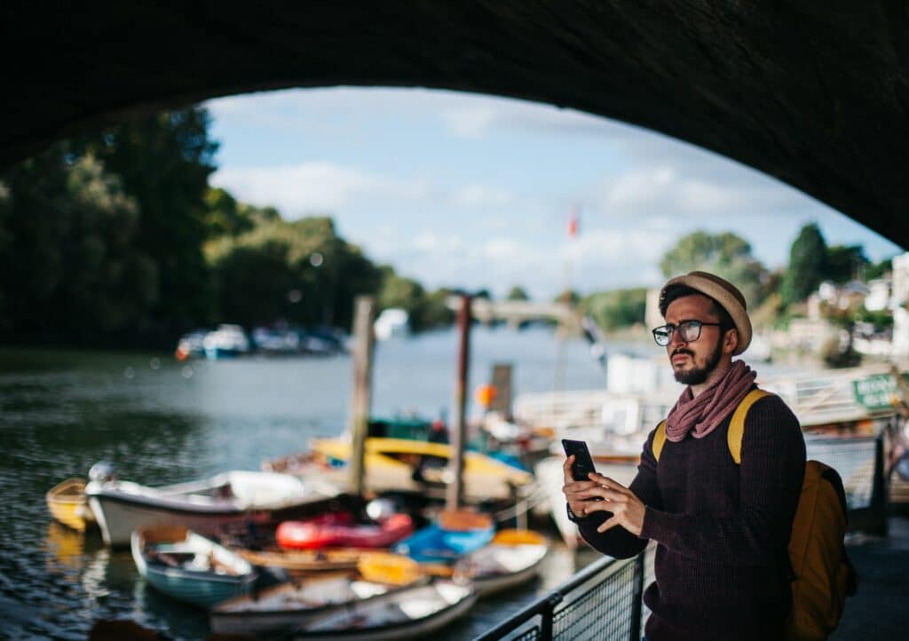 homem confuso olhando o celular tentando se localizar no parque em Richmond, na Inglaterra, com barcos de fundo em um lago, o chip internacional pré-pago te ajuda a se localizar em qualquer lugar