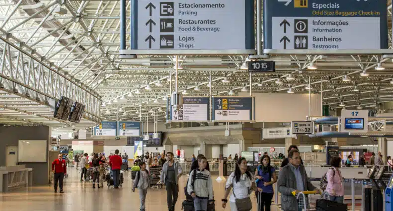 Saguão dentro do Aeroporto do Galeão com diversas pessoas andando com malas
