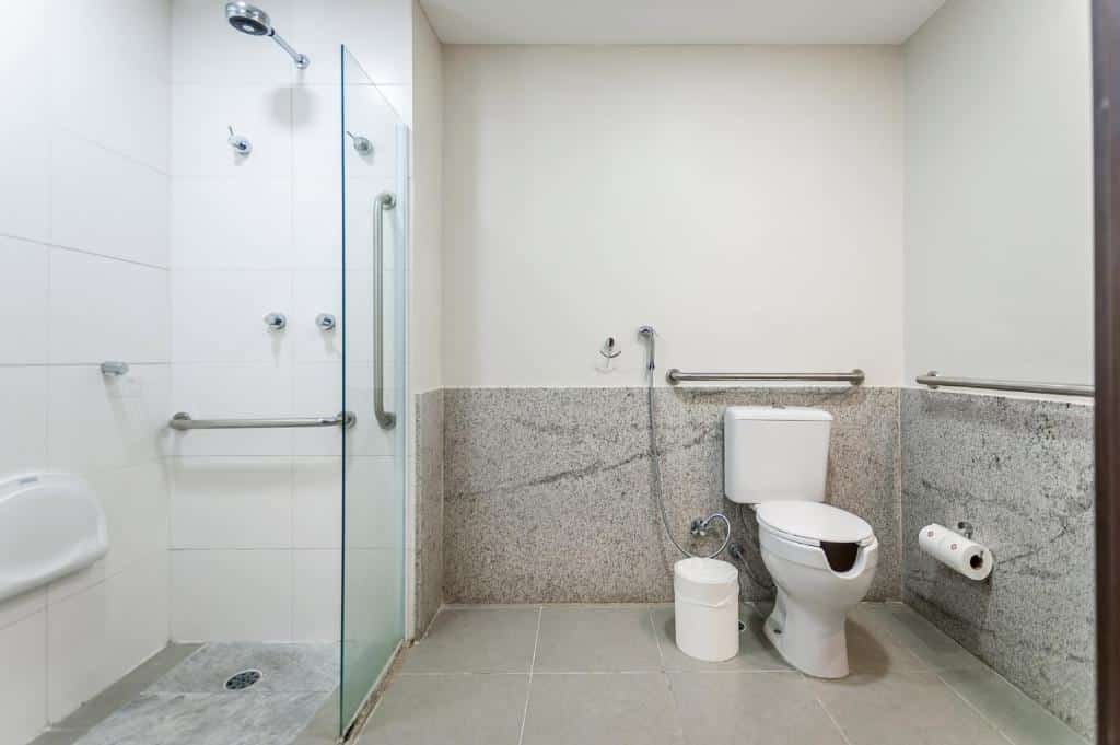 Banheiro com acessibilidade do Intercity Maceio, com barras de apoio na lateral e acima do vaso, e na área do banho tem barras de apoio na parede do chuveiro e na lateral. O espaço é amplo e não tem degrau