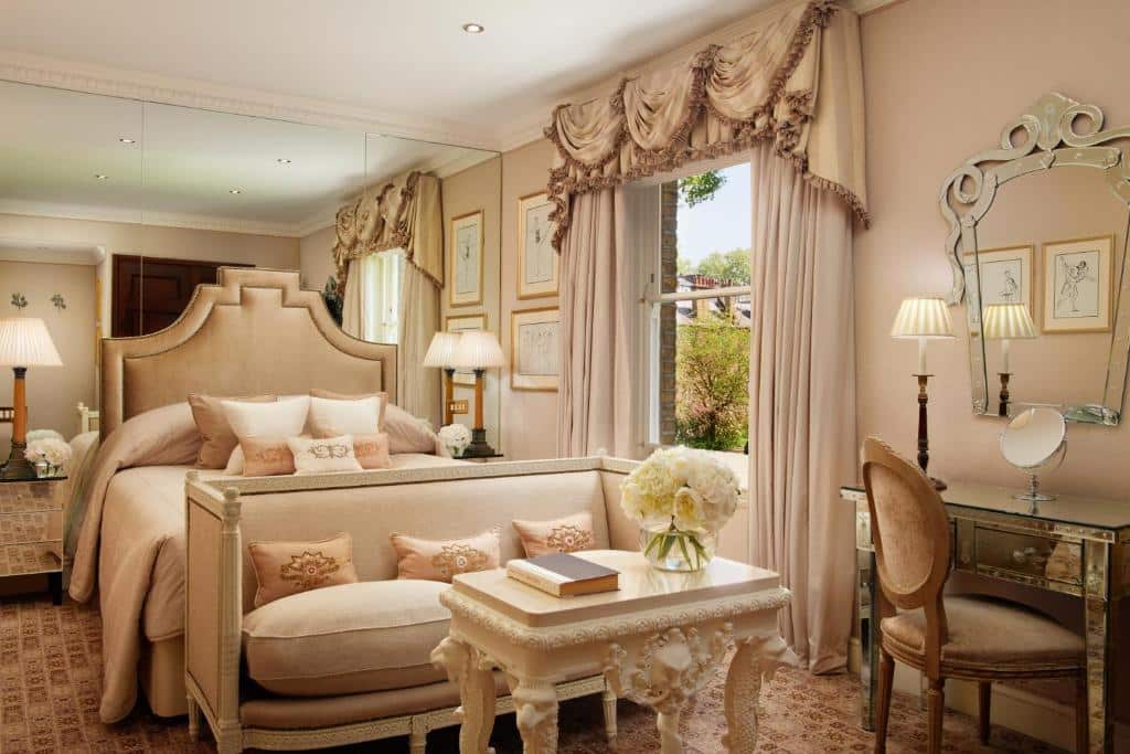 Quarto do Egerton House em estilo europeu, com duas janelas com cortinas, uma cama de casal com muitas almofadas, um sofá com dois lugares, uma mesinha de centro com um vaso de flor, além de uma penteadeira