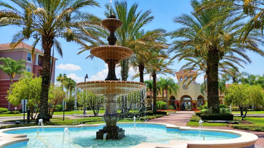 entrada do local em que está o apartamento Majestic Retreat, uma das opções de onde ficar em Orlando, com um caminho e uma fonte de água e palmeiras na beira
