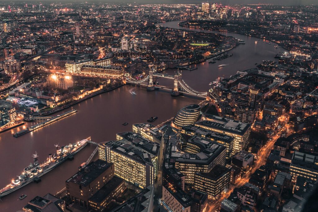 Vista aérea de Londres com diversos prédios iluminados e famosa Ponte de Londres cortando o rio Tâmisa que conta com algumas embarcações