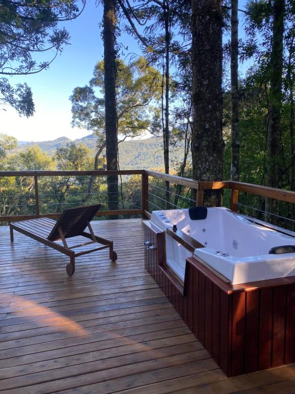 área aberta com um deque de madeira, uma espreguiçadeira e uma banheira de hidromassagem com vista para o vale coberto de vegetação natural