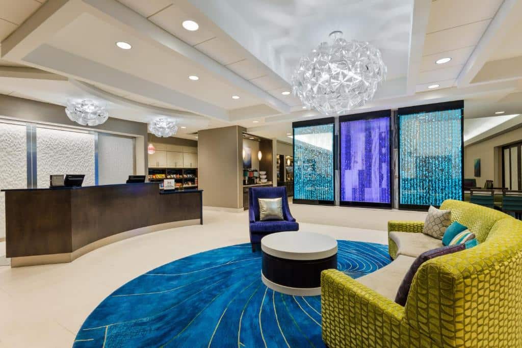 lounge colorido do Homewood Suites by Hilton Orlando-Nearest to Universal Studios com tapete redondo azul marmorizado, poltronas verdes e luminárias em ninhos acima, há recepção e três quadros decorativos de vidro