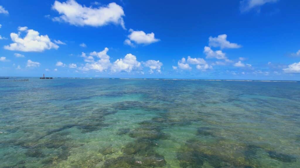 Mar raso e transparente, mostrando corais ao fundo, durante um dia ensolarado com poucas núvens em Maceió.