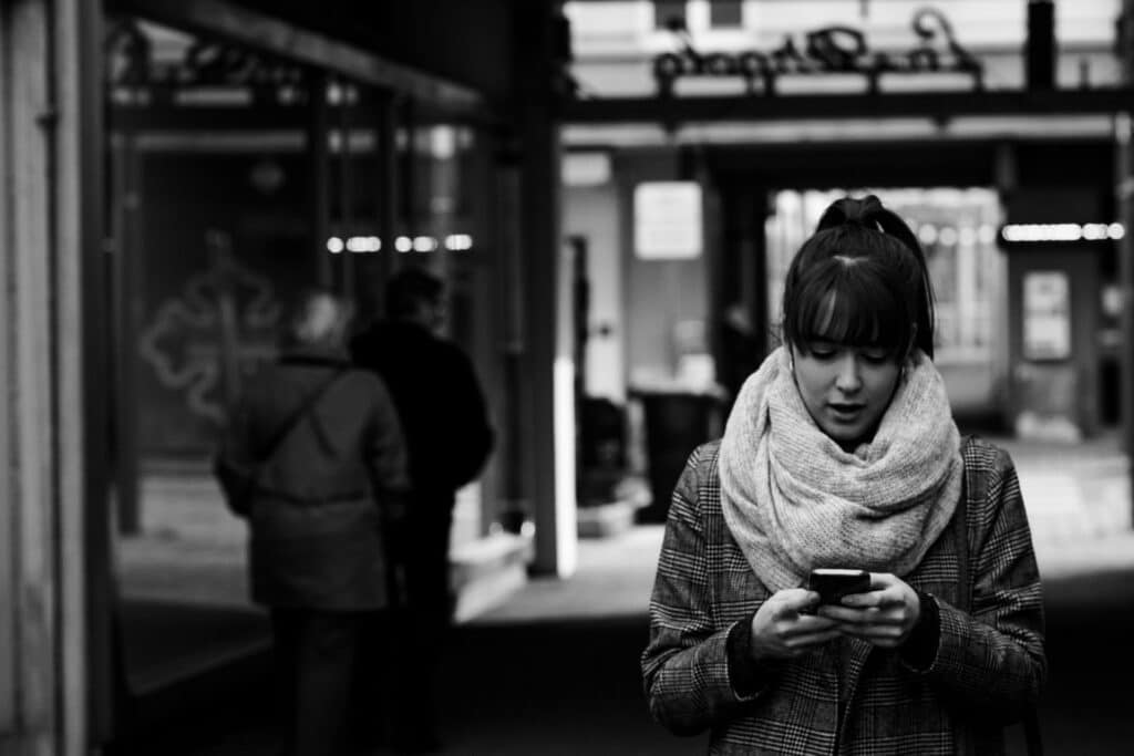 Uma mulher com um casaco e um cachecol usando um celular em uma rua