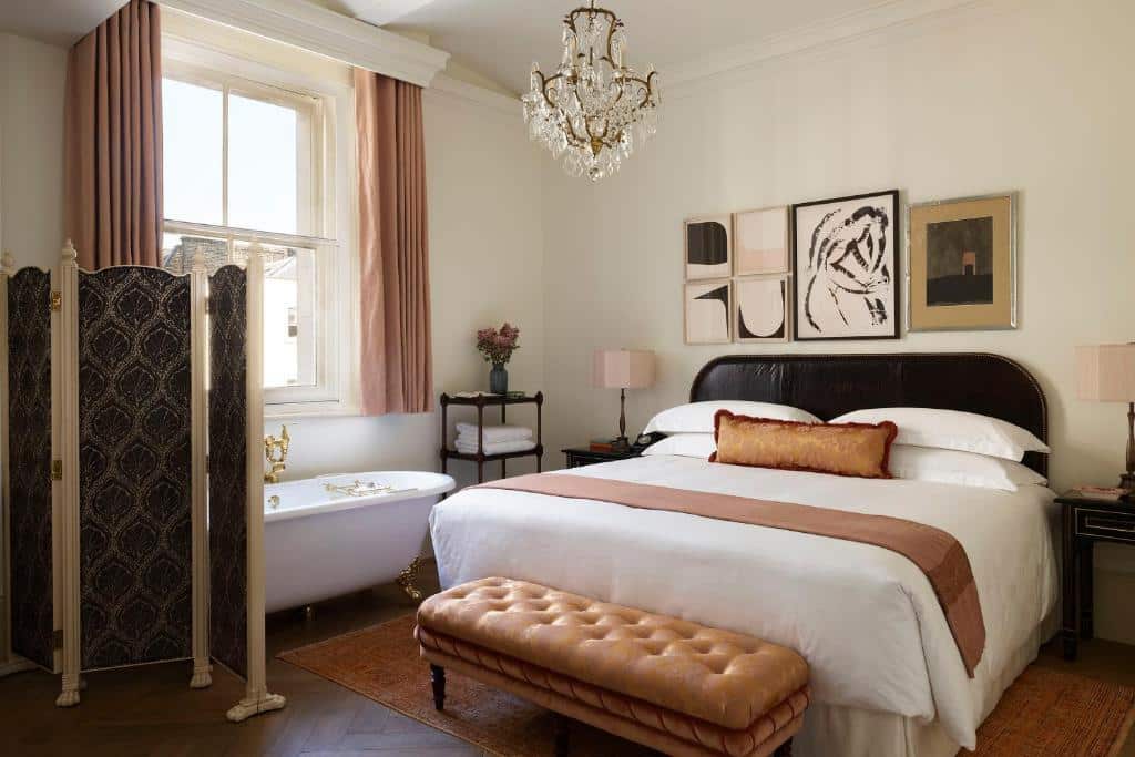 Quarto do NoMad London  com uma cama de casal, uma banheira, uma janela ampla com cortinas, quadros nas paredes, um lustre que imita um flor, e um tapete em tom de cobre