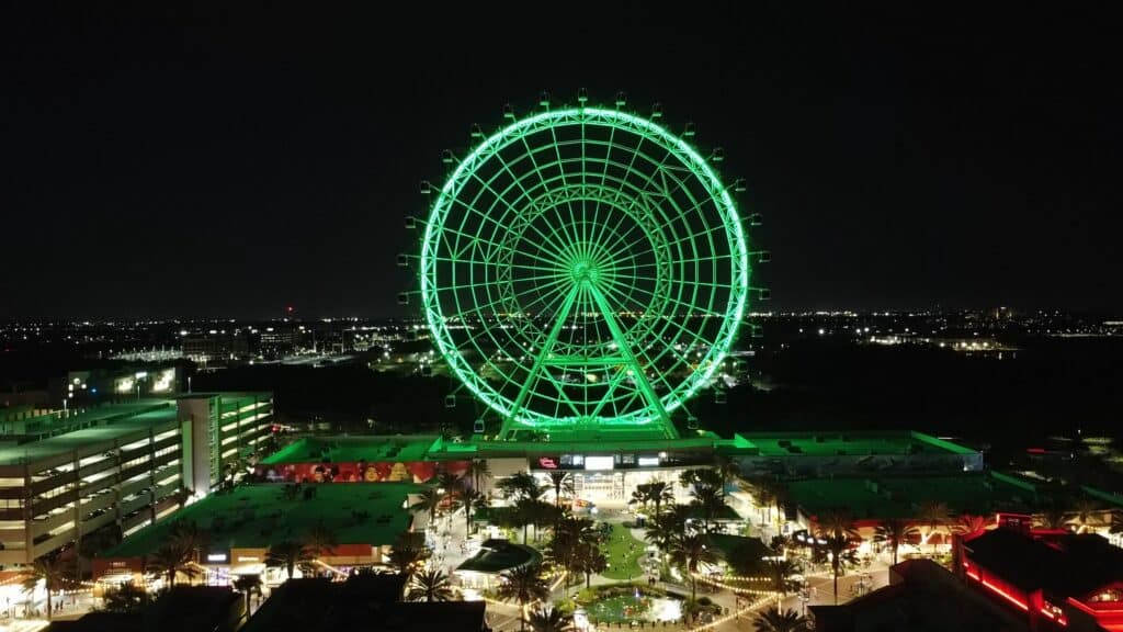 Orlando Eye, uma roda-gigante com luzes verdes neon acima de um parque com árvores e quadras abaixo, na International Drive, uma das opções de onde ficar em Orlando