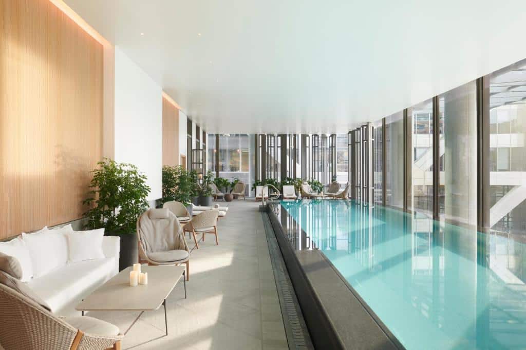 Piscina coberta do Pan Pacific London com janelas amplas, e no deck há sofás e poltronas, além de vasos de plantas, para representar os melhores hotéis em Londres