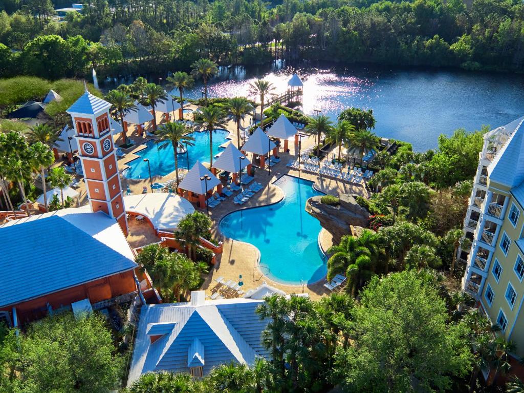 piscinas sinuosas com um grande lago na frente no Hilton Grand Vacations Club SeaWorld Orlando, uma das opções de onde ficar em Orlando, ainda há várias árvores, cadeiras e construções que parecem castelinhos