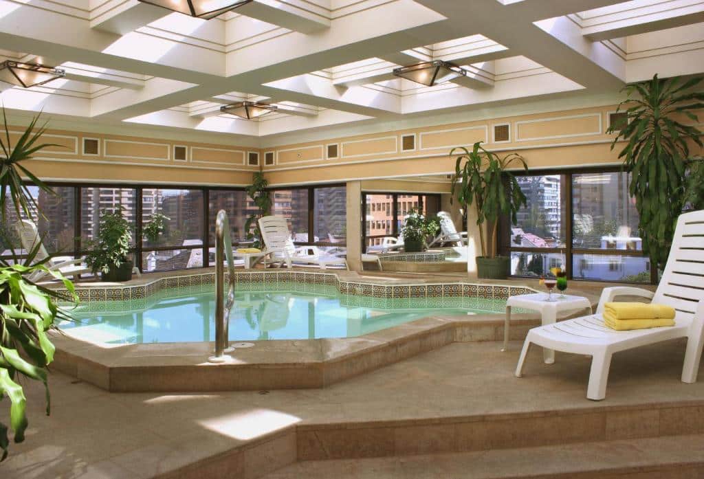 Piscina coberta do Hotel Regal Pacific com cadeiras  brancas em volta e alguns vasos de plantas no ambiente.