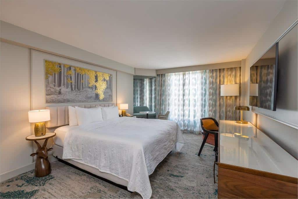 quarto do Castle Hotel, Autograph Collection by Marriott, em Orlando, com cama de casal e detalhes no carpete marmorizado, com decoração chique e bancada com mesa e sofá azul, há uma janela grande e cortinas leves
