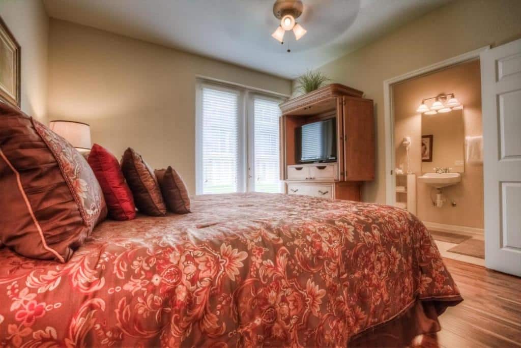 quarto do Majestic Retreat com cama de casal com colchas avermelhadas, luminária de teto, espelho, guarda-roupa com uma tv e uma janela de vidro