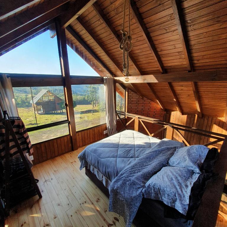 interior da cabana 16 com vista da suíte, mostrando uma cama de casal e as janelas amplas de vidro com vista para a natureza e outras construções da região