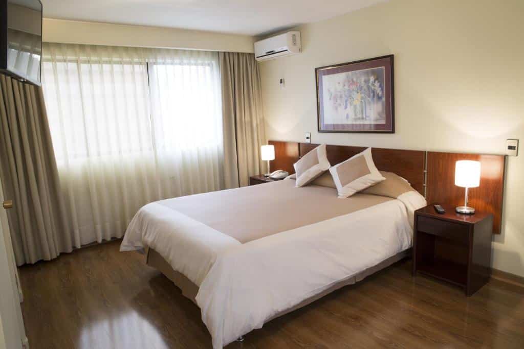 Quarto do Hotel Diego de Velazquez com cama de casal ao centro do quarto duas cômodas de madeira ao lado da cama com luminárias.