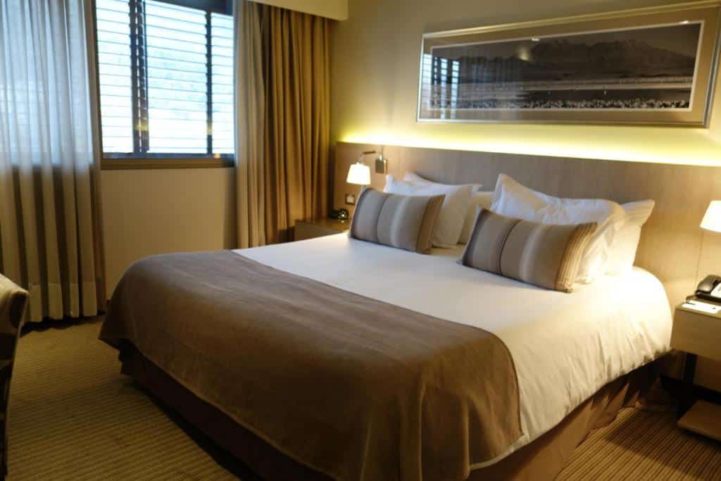 Quarto do Hotel Los Españoles Plus com cama no centro do quarto e duas cômodas de madeira ao lado da cama com luminária.