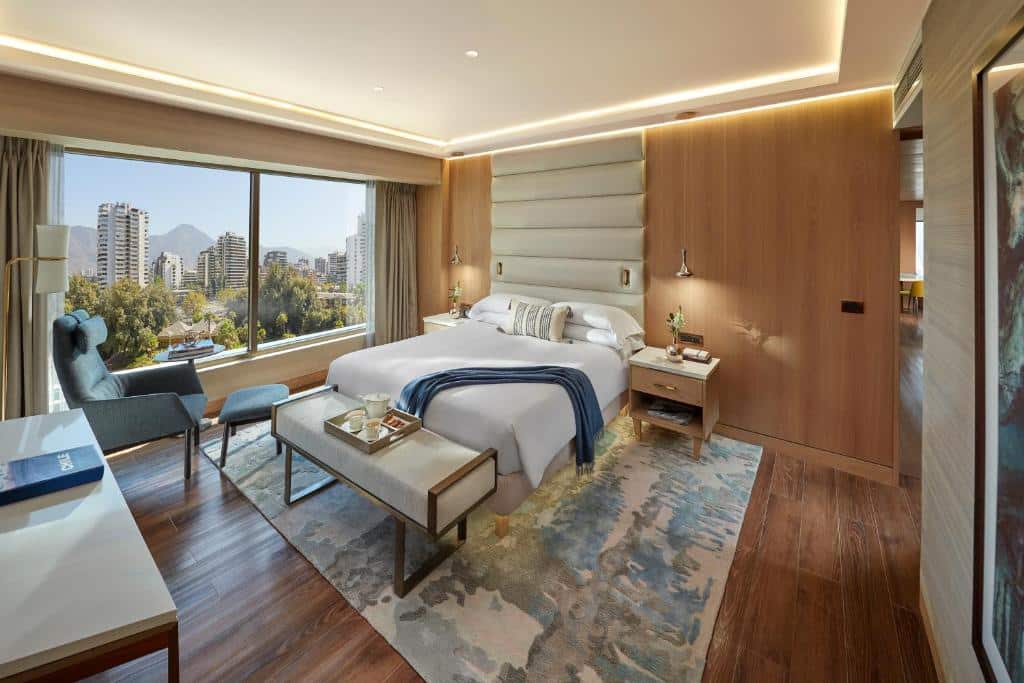 Quarto do Mandarin Oriental com cama de casal no centro, duas cômodas ao lado da cama e, em frente a cama, uma poltrona azul.