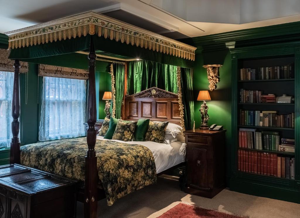 Quarto super decorado do The Rookery em estilo vitoriana em tons de verde escuro, uma cama de casal com um bangalô, duas janelas com cortinas, duas mesinhas de cabeceira com abajures, uma estante com livros e um tapete