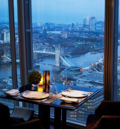 Área de refeições do Shangri-La The Shard, London com uma janela panorâmica dando vista para a cidade, há uma pequena mesa com dois lugares, para representar os melhores hotéis em Londres