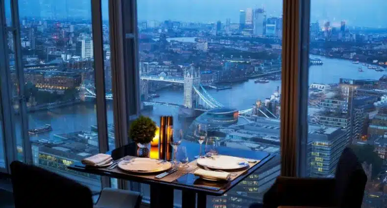 Área de refeições do Shangri-La The Shard, London com uma janela panorâmica dando vista para a cidade, há uma pequena mesa com dois lugares, para representar os melhores hotéis em Londres