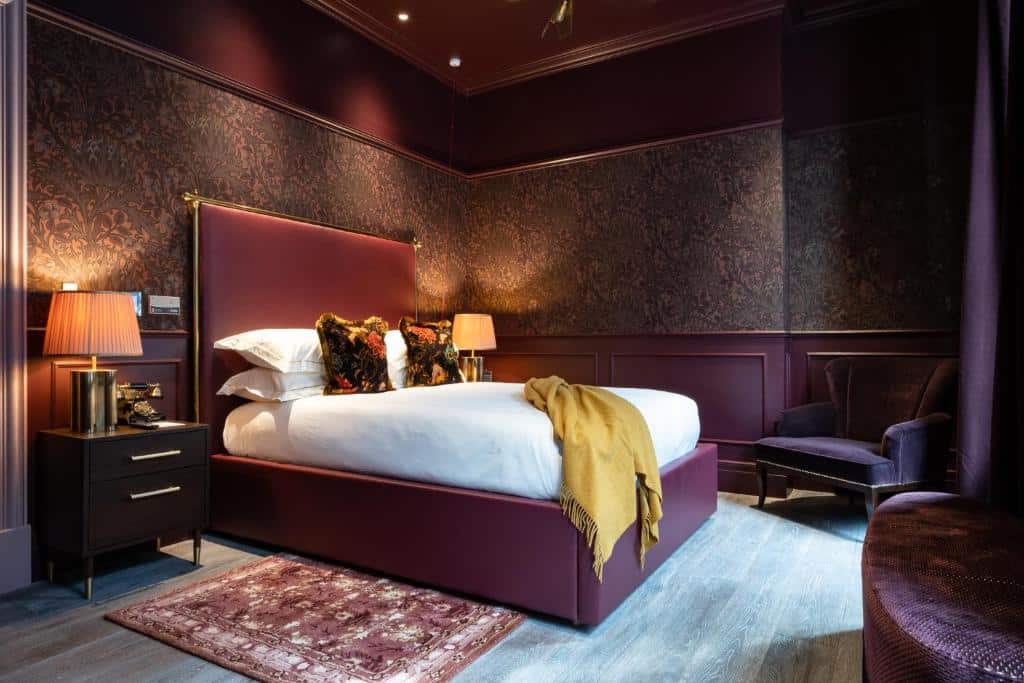 Quarto do Sun Street Hotel inteiro decorado em tons de roxo, uma cama de casal, duas poltronas em tom de vinho, iluminação indireta e duas mesinhas de cabeceira com abajures
