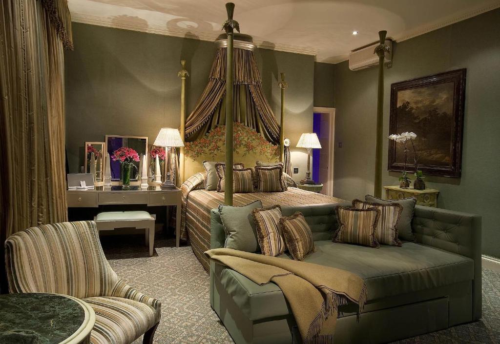 Quarto do The Chesterfield Mayfair decorado em tons de verde e bege, há uma cama de casal, um sofá com dois lugares, uma penteadeira, uma janela ampla, uma poltrona e um quadro