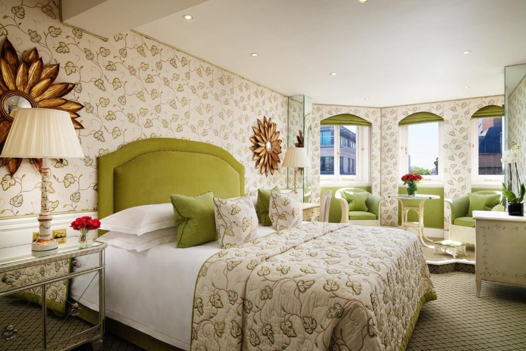 Quarto do The Chesterfield Mayfair com cama de casal, três janelas, duas poltronas, tudo decorado em verde claro, roupas de cama florais e um carpete verde claro com marrom