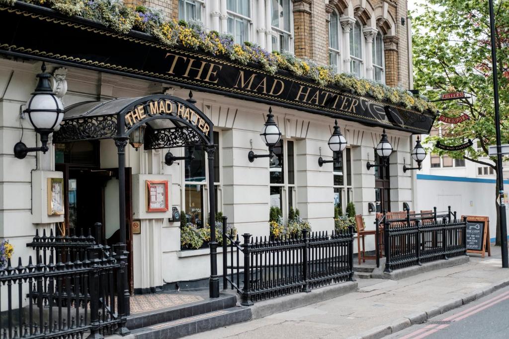 Fachada do The Mad Hatter Hotel com uma fachada coberta por flores, há grades pretas na entrada, com lustres e uma entrada bem europeia, para representar os melhores hotéis em Londres