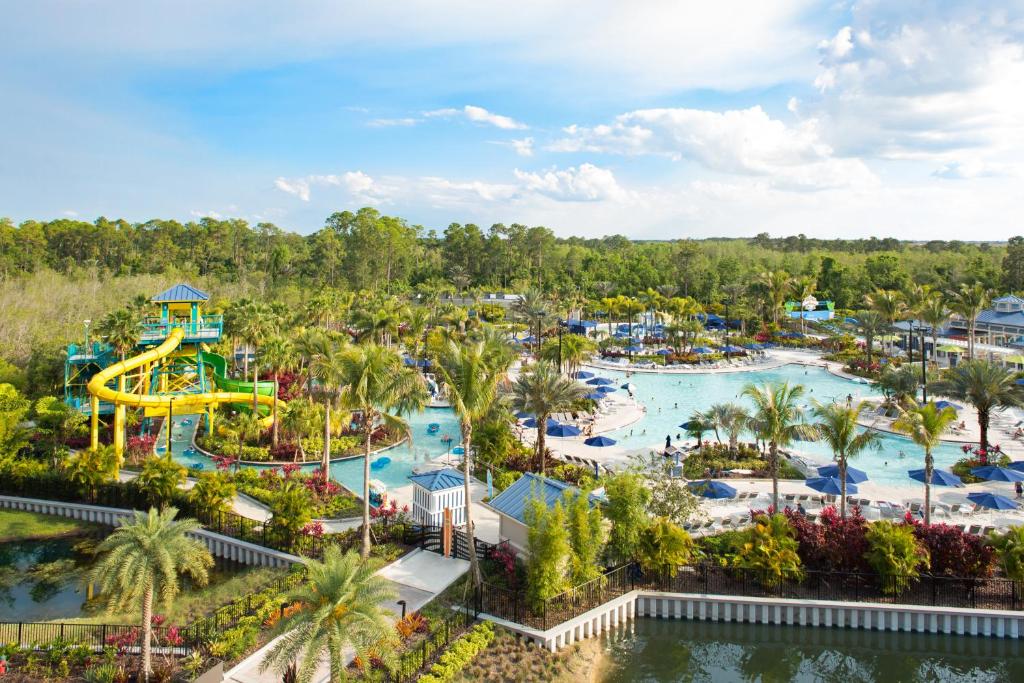 vista das piscinas do The Grove Resort & Water Park Orlando com tobogã colorido e muitas palmeiras ao redor, há ainda mesinhas e cadeiras distribuídas