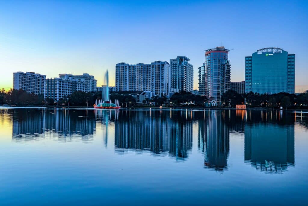 vista da cidade de Orlando com prédios refletidos no Lake Eola com uma fonte colorida enorme que joga um jato alto de água