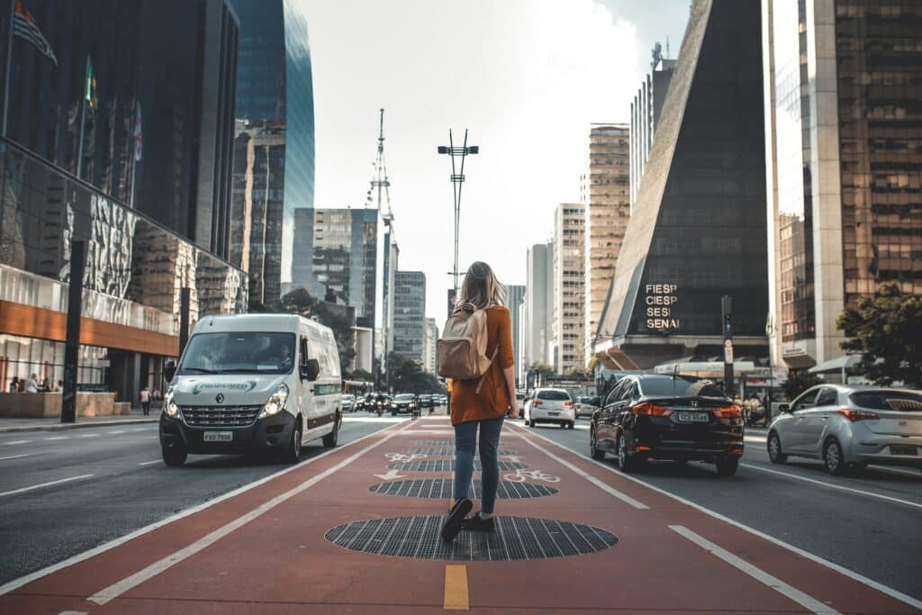 mulher de costas com uma mochila na Avenida Paulista, em São Paulo, há carros passando e prédios importantes, em uma passarela vermelha, para ilustrar o post chip internacional funciona no Brasil