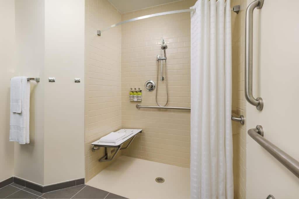banheiro com adaptações para PcDs, como box de cortinas, barras de apoio nas paredes,  cadeira de banho e chuveirinho em um ambiente amplo, no Candlewood Suites - Orlando - Lake Buena Vista, an IHG Hotel, um dos hotéis perto de Lake Buena Vista em Orlando