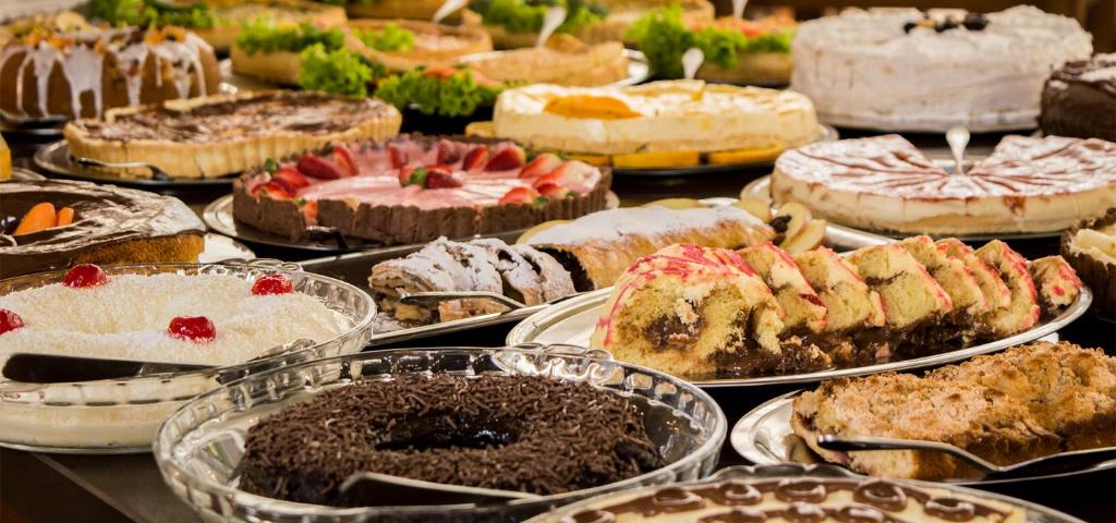 mesa de alimentos do Sky Serra Hotel com diversos bolos e pães espalhados até se perder de vista