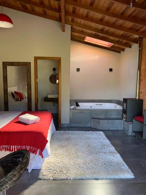 interior do Chalé dos Pássaros em Gramado com uma cama de casal à esquerda, uma banheira de hidromassagem à direita e uma lareira ao lado da banheira.