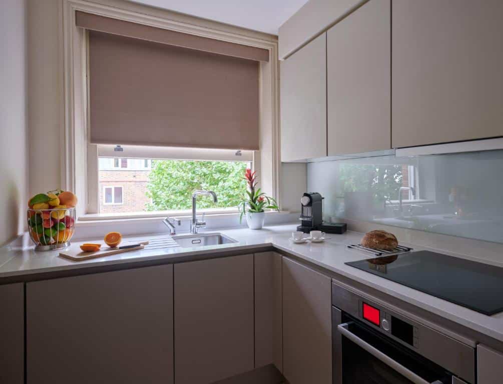 Cozinha do The Apartments by The Sloane Club com uma janela com persiana, um forno, uma bancada com uma cafeteira, um vaso de planta e uma cesta com frutas