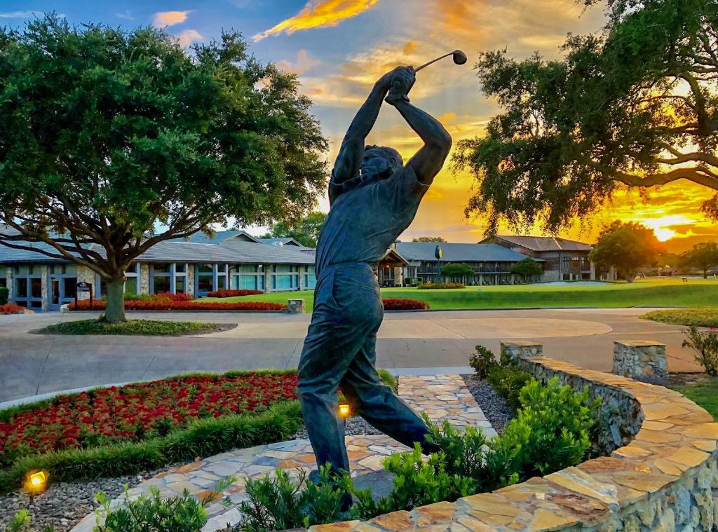 estátua de um jogador de golfe em um jardim com flores coloridas e grama bem aparada, ao fundo, as varandas dos quartos amplos do Arnold Palmer's Bay Hill Club & Lodge, um dos hotéis de luxo em Orlando
