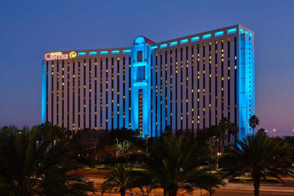 fachada iluminada de azul do Rosen Centre Hotel Orlando Convention Center, um dos hotéis na International Drive em Orlando, com janelinhas acesas e palmeiras na frente