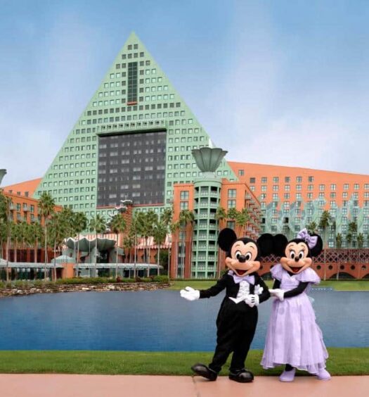 Mickey e Minnie em frente a um lago com a fachada do Walt Disney World Dolphin ao fundo, um dos melhores hotéis em Orlando