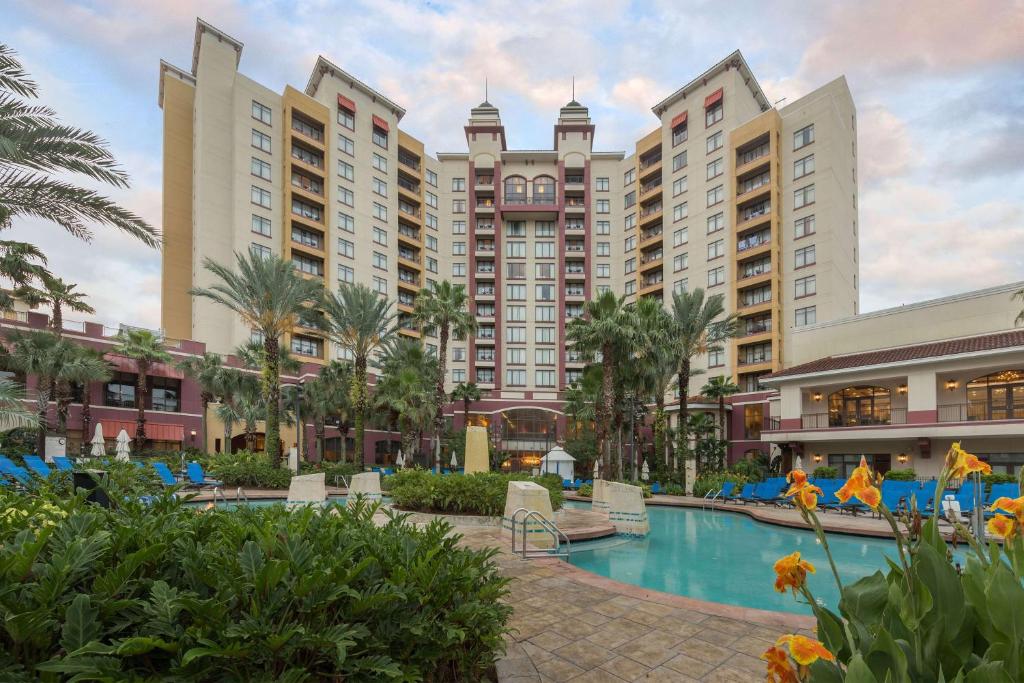 fachada em tons bege e vermelho com várias janelinhas do Wyndham Grand Orlando Resort Bonnet Creek um dos hotéis românticos em Orlando, e a piscina abaixo, sendo uma grande de bordas sinuosas e duas de hidro menores, com flores amarelas ao redor