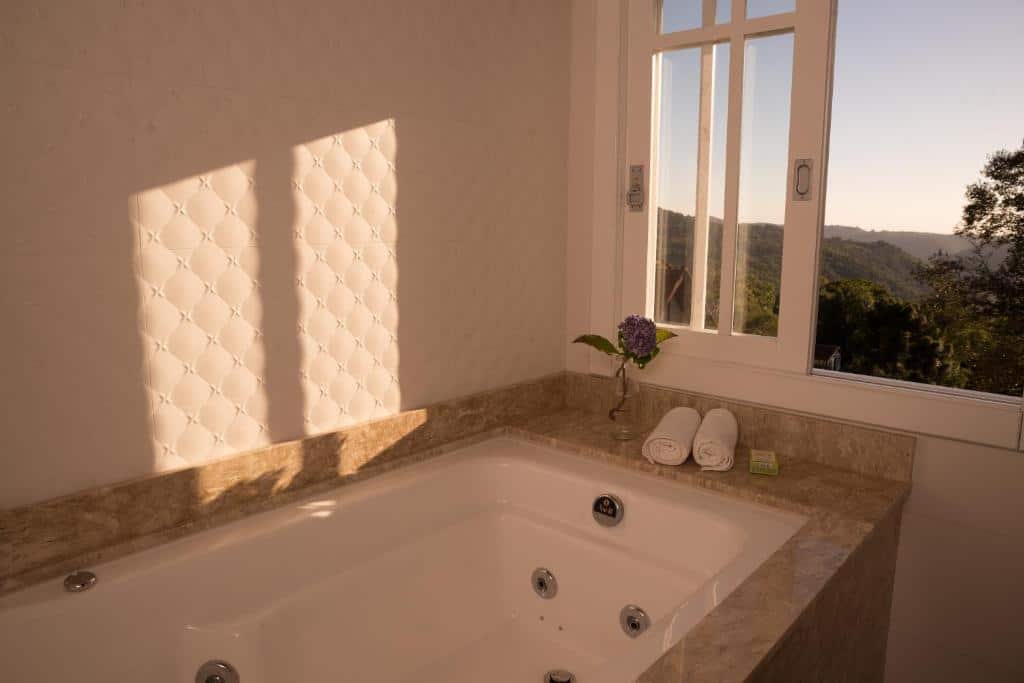 banheira de hidromassagem da Pousada La Vista com uma janela à direita e a vista do pôr do sol na serra gaúcha