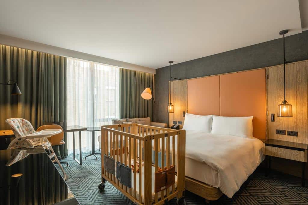 Quarto do Hilton London Bankside com uma cama de casal, um berço de madeira, uma janela com cortinas e um carpete, para representar hotéis para família em Londres
