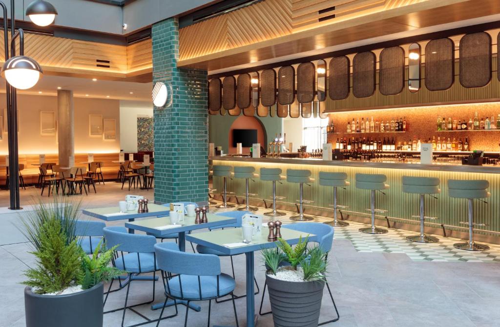 Salão de refeições no Holiday Inn London Heathrow - Bath Road, an IHG Hotel com um bar com banquetas, mesas quadradas e cadeiras estão no espaço que é aberto, nos arredores há mesas na parte coberta também