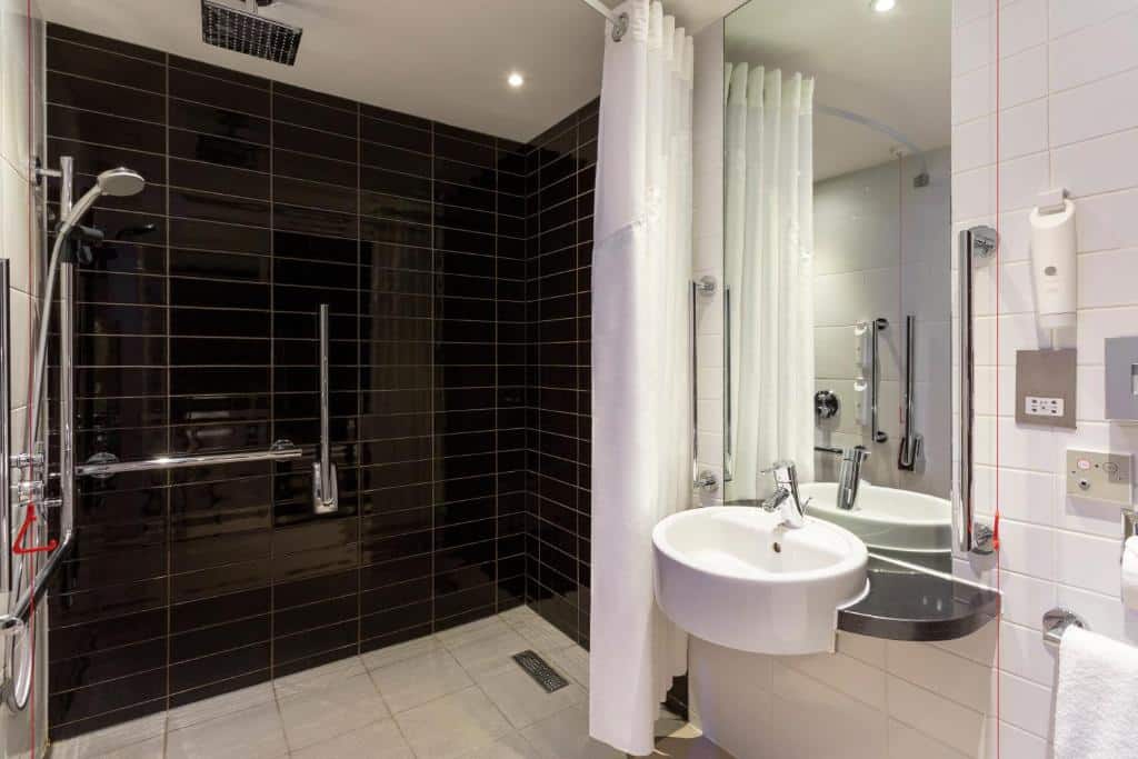 Banheiro adaptado do Holiday Inn Express Southwark, an IHG Hotel com barras de apoio, box sem vidro, pia mais baixa, cordão de emergência e um espelho