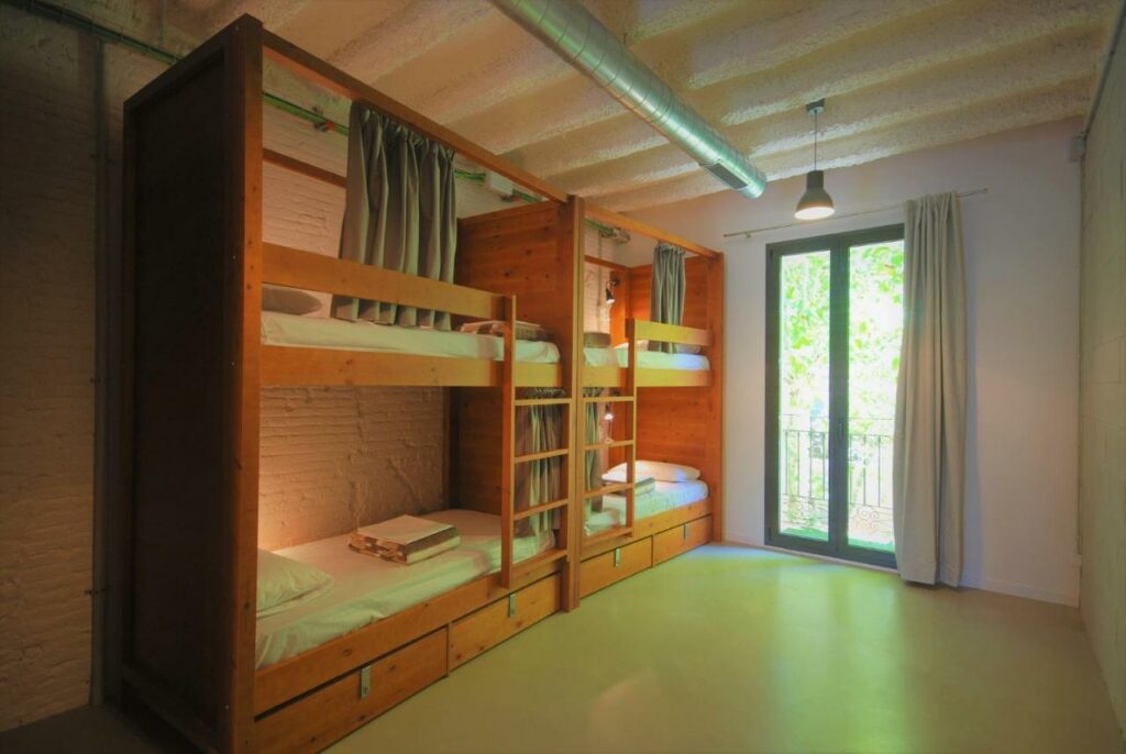 Duas beliches em um quarto do Ten To Go Hostel. Há roupa de cama e cortinas em cada uma das quatro camas. Uma porta de vidro com cortina leva à varanda.