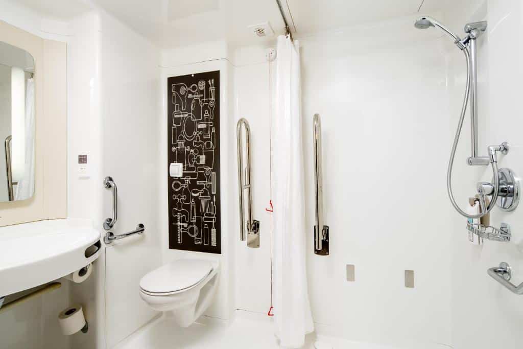 Banheiro adaptado do ibis London City – Shoreditch com barras de apoio, cordão de emergência e box sem vidro
